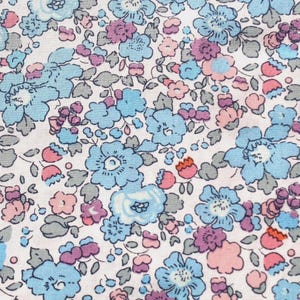May include: Close-up of a floral fabric with a white background. The pattern features small, stylized flowers in shades of light blue, pink, and purple, with gray-green leaves. The design is densely packed and detailed.