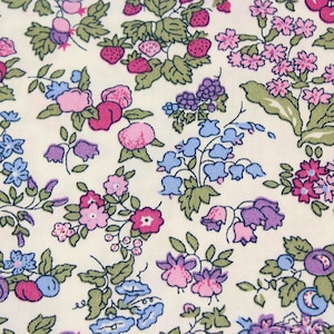 May include: A cream-colored fabric featuring a repeating botanical print of small strawberries, cherries, and various clusters of pink, purple, and light blue flowers with green leaves. The pattern is dense and evenly distributed across the surface.