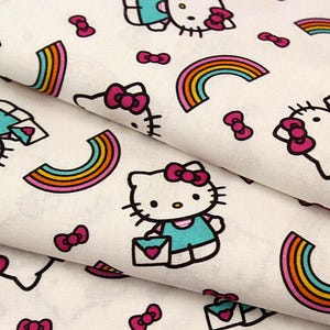 May include: White fabric with a repeating pattern of Hello Kitty characters, bows, and rainbows. The Hello Kitty figures are outlined in black, with pink bows and turquoise dresses. The rainbows have orange, yellow, and blue stripes.