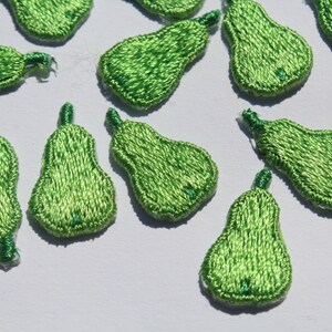 May include: A collection of green pear-shaped fabric embellishments. The pears are made of a soft, textured fabric and have a slightly three-dimensional appearance.