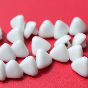 May include: A group of white plastic triangle-shaped buttons. The buttons are arranged in a random pattern on a red surface.