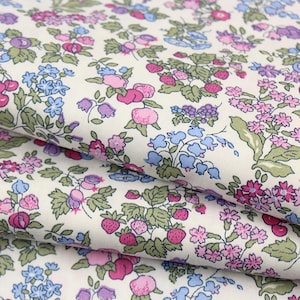 May include: A white fabric featuring a dense, repeating botanical print of small pink and purple flowers, light blue bell-shaped blossoms, green leaves, and clusters of red strawberries and cherries scattered across the surface in a continuous pattern.