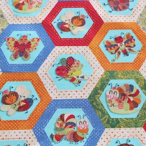 May include: A colorful fabric with a repeating pattern of hexagonal shapes. Each hexagon features a different whimsical insect or animal, including butterflies, ladybugs, caterpillars, and snails. The fabric is a patchwork of different colors, including red, blue, green, yellow, and orange.
