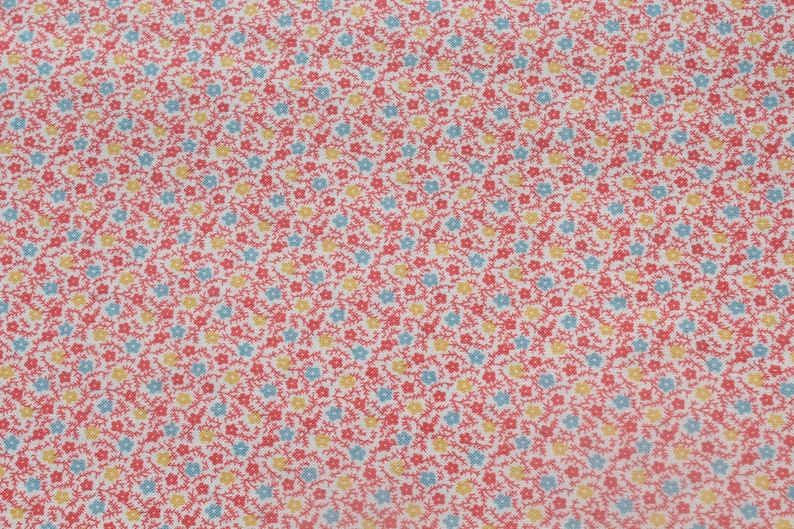 May include: Close-up of a fabric with a repeating floral pattern. The design features small red flowers, light blue and yellow blossoms, and thin red stems against a white background. This fabric is suitable for various sewing and crafting projects.