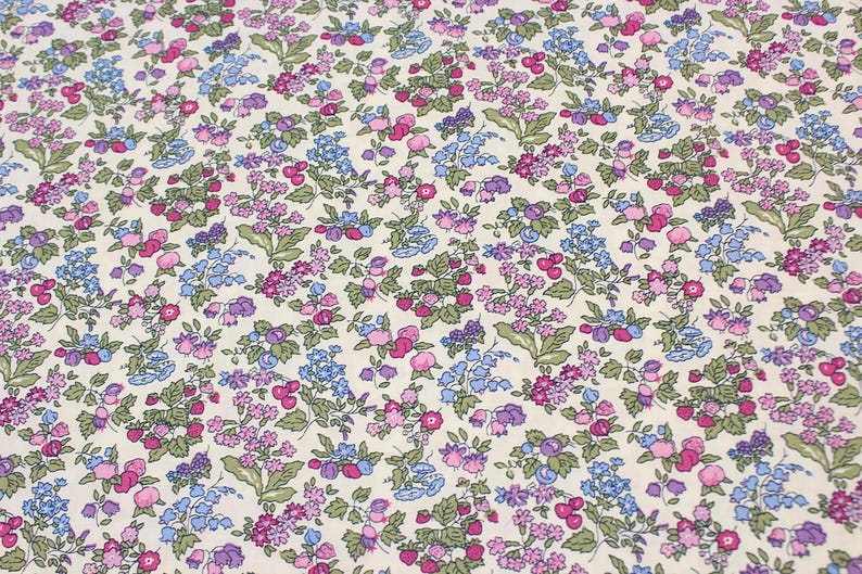 May include: A fabric featuring a dense, repeating floral pattern on a cream-colored background. The design consists of small pink, purple, and blue flowers interspersed with green leaves and stems, creating a continuous botanical print across the surface.