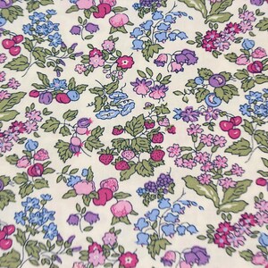 May include: A cream-colored fabric featuring a dense, repeating botanical print. The pattern consists of small pink, purple, and blue flowers, green leaves, and clusters of red strawberries and dark blue berries scattered across the surface.