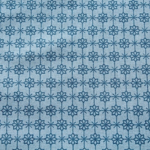 May include: Close-up of a light blue fabric with a repeating pattern of dark blue floral and star-like shapes. The design is arranged in a grid-like formation, creating a textured appearance. The fabric appears to be cotton or a similar material.