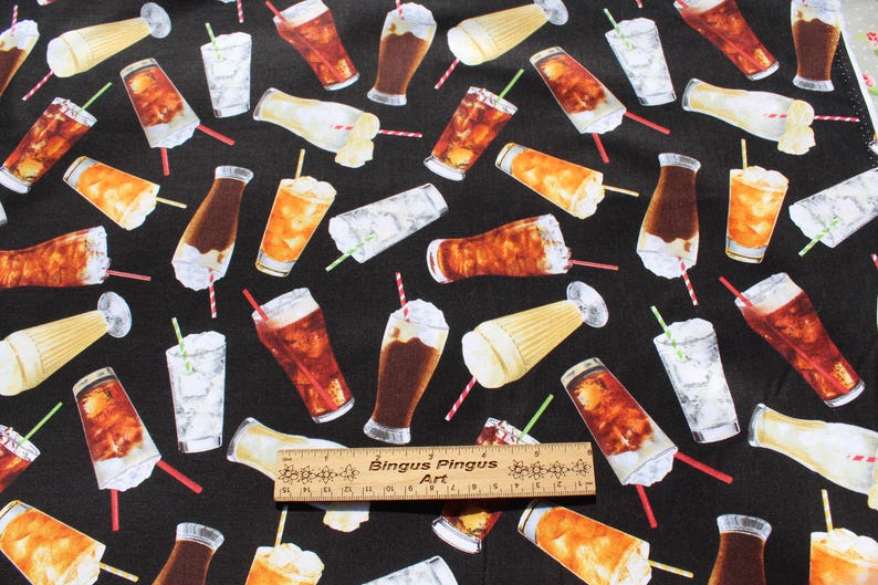 May include: Black fabric featuring a repeating pattern of drinks, including cola, iced tea, and milkshakes. The drinks are in glasses and bottles, with straws and whipped cream. A wooden ruler with text is at the bottom.