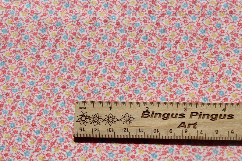 May include: A patterned fabric featuring a repeating floral design in red, yellow, and blue on a white background. A wooden ruler, marked in inches, with the text "Bingus Pingus Art" is placed on the fabric.