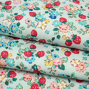 May include: A light blue fabric featuring a repeating pattern of small red strawberries, pink flowers, and bright blue blossoms with green leaves. The textile has a woven texture and displays a dense, colorful botanical print across the surface.