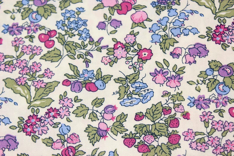 May include: A fabric featuring a repeating botanical print on an off-white background. The pattern consists of small pink, purple, and blue flowers, green leaves, red cherries, and small red strawberries scattered across the entire surface.