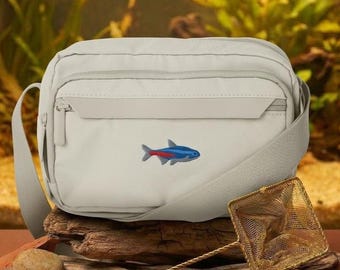 May include: A light grey crossbody bag featuring an embroidered neon tetra fish with a blue and red body. The bag has a zippered front pocket and an adjustable shoulder strap. A small gold-toned metal mesh fish net is positioned in front.