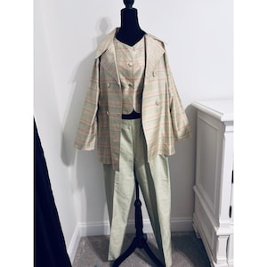 以下が含まれることがあります： ダブルブレストのジャケット、ボタン付きベスト、パンツの3点セット。ジャケットとベストはベージュをベースに、落ち着いた緑とオレンジの横縞模様が入っています。パンツは無地のライトグリーンです。
