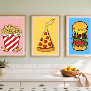 Puede incluir: Tres láminas enmarcadas con coloridas ilustraciones de comida. La lámina de la izquierda muestra palomitas en un cubo de rayas rojas y blancas sobre fondo rosa, la central una porción de pizza de pepperoni sobre amarillo y la derecha una hamburguesa sobre azul.