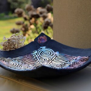 Könnte beinhalten: Eine schwarze Keramik-Servierplatte mit einem dekorativen Design aus wirbelnden Linien und Kreisen in schimmerndem Silber, Rosa und Blau.