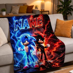 May include: A rectangular fleece blanket featuring a graphic print of Sonic the Hedgehog surrounded by blue lightning and Shadow the Hedgehog surrounded by red lightning, with the word NAME printed in a bold, stylized font at the top.