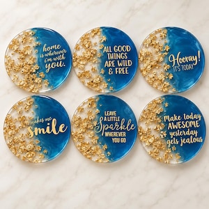 May include: A set of six circular coasters featuring a deep blue and translucent resin design with embedded gold leaf flakes. Each coaster displays gold text: home is wherever i'm with you, ALL GOOD THINGS ARE WILD & FREE, Hooray! IT'S TODAY, makes me smile, LEAVE A LITTLE Sparkle WHEREVER YOU GO, and Make today AWESOME yesterday gets jealous.