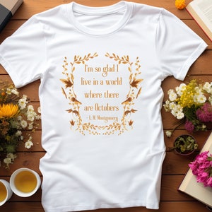 May include: White t-shirt with a gold leaf design and a quote from L.M. Montgomery: "I'm so glad I live in a world where there are Octobers."