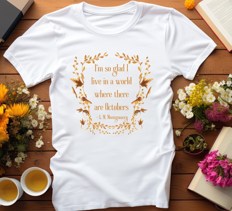 May include: White t-shirt with a gold leaf design and a quote from L.M. Montgomery: "I'm so glad I live in a world where there are Octobers."