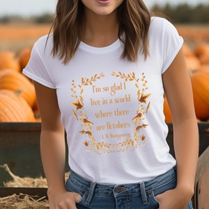 May include: White t-shirt with a gold graphic print of a quote by L.M. Montgomery. The quote reads "I'm so glad I live in a world where there are Octobers".