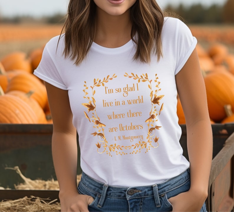 May include: White t-shirt with a gold graphic print of a quote by L.M. Montgomery. The quote reads "I'm so glad I live in a world where there are Octobers".