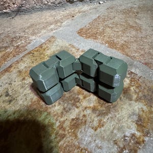 May include: An olive green articulated fidget toy constructed from multiple connected geometric blocks. The object features a series of hinged segments that allow for flexible movement and manipulation, showcasing a matte finish and visible 3D printed texture.