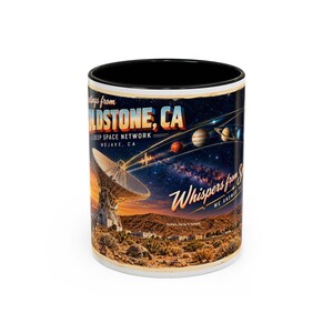 May include: A ceramic mug with a black interior and rim, featuring a graphic of the Goldstone Deep Space Network in the Mojave Desert. The design includes a large satellite dish, a starry night sky with planets, and text reading Greetings from Goldstone, CA, Deep Space Network, Mojave, CA, and Whispers from Space.