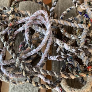May include: A pile of colorful, braided rope made from recycled fabric scraps. The rope is a mix of white, gray, black, and brown colors.