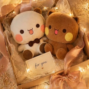 May include: Two plush bear toys, one white with a brown bowtie and one brown, sit inside a gift box lined with tissue paper. A small rectangular card with the text "for you" and a tiny heart icon is placed in front of the two soft stuffed animals.
