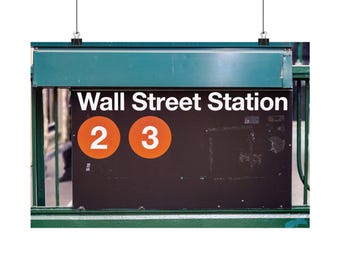 May include: A rectangular black subway sign with white text reading Wall Street Station. Two orange circular icons featuring the white numbers 2 and 3 are displayed on the sign. The sign is mounted on a green metal frame and suspended by wires.