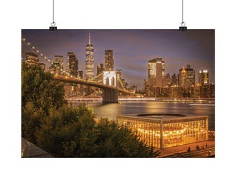 May include: A wall art print featuring a night view of the New York City skyline, the Brooklyn Bridge, and Jane's Carousel illuminated in gold. The scene captures the East River, dark trees in the foreground, and skyscrapers under a twilight sky.