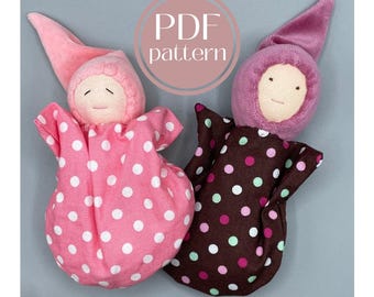 Può includere: Due bambole di stoffa fatte a mano con tessuto a pois. Le bambole indossano abiti con cappuccio rosa e marrone. Le bambole sono su uno sfondo grigio. Il testo "PDF pattern" è in un cerchio sopra le bambole.