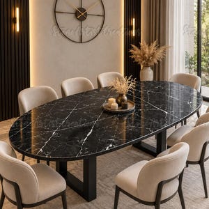 Puede incluir: Una mesa de comedor ovalada con tablero de mármol negro con vetas blancas, apoyada sobre una base de metal negro. Ocho sillas tapizadas en tela beige claro con marcos oscuros rodean la mesa. Una bandeja redonda con velas se sitúa en el centro.