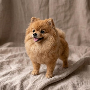 May include: A needle-felted Pomeranian dog figurine with dense, textured golden-brown fur, small upright ears, dark eyes, and a black nose. The sculpture features an open mouth showing a pink tongue, standing in a realistic pose.