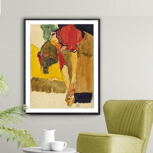 Puede incluir: Una pintura al agua de una persona con una camisa roja, tumbada sobre una superficie amarilla y marr&oacute;n. Las piernas de la persona est&aacute;n extendidas y los brazos doblados por los codos. La pintura est&aacute; enmarcada en negro.