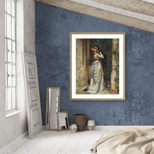 May include: A framed print of a romantic scene. The artwork depicts a couple embracing near a gate. The woman wears a white dress with blue accents, and the man is in a dark suit. The frame is light brown, and the background is a textured blue wall.