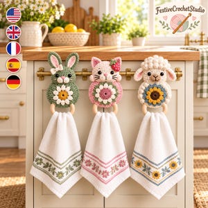 May include: Three crochet kitchen towel holders featuring a green bunny with a daisy, a pink cat with a strawberry, and a white sheep with a sunflower. Each holder includes a wooden ring and a white towel with a matching floral embroidered border.