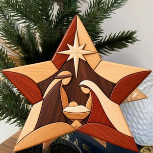 Könnte beinhalten: Ein sternförmiger Holzschmuck mit einer Intarsien-Krippenszene. Das Design verwendet verschiedene Nuancen von hellem, mittlerem und dunklem Holz, um zwei Figuren darzustellen, die sich über eine zentrale Krippe beugen.