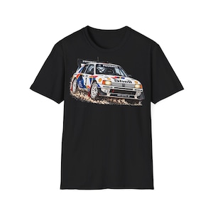 Op de afbeelding: Een zwart t-shirt met korte mouwen en een grafische print van een witte Peugeot 205 Turbo 16 rallyauto. De auto toont het nummer 3, Shell- en Michelin-branding, en wordt afgebeeld terwijl deze vuil opwerpt op een racebaan.