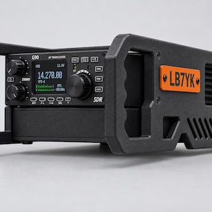 May include: A black Xiegu G90 HF transceiver housed in a protective frame with integrated handles. The front panel features a digital display showing 14.270.00, control knobs, and buttons. An orange rectangular plate on the side is labelled LB7YK.