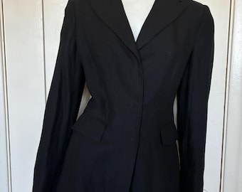 May include: A solid black blazer featuring a notched lapel, long sleeves, and two front flap pockets. The jacket is tailored with a structured fit, a single-button closure, and a straight hemline, displayed on a white mannequin torso.