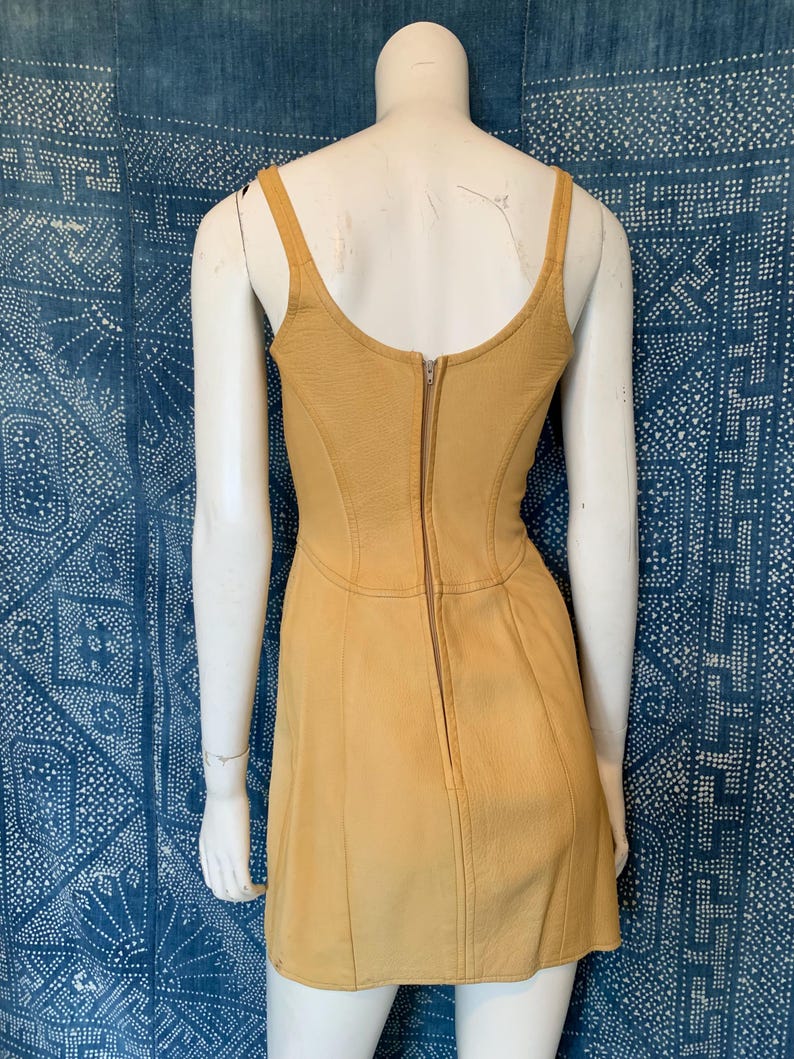 May include: A mustard yellow sleeveless dress featuring a scoop neckline, a fitted bodice with vertical seam detailing, and a central vertical zipper closure running down the back. The garment is displayed on a mannequin, showcasing a structured silhouette.