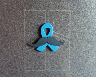 Peut inclure: Un ruban de sensibilisation bleu clair à la finition lisse, surmonté d'une moustache noire superposée horizontalement au centre. Le design est plat et symétrique, combinant une boucle de ruban classique avec un motif de pilosité faciale.