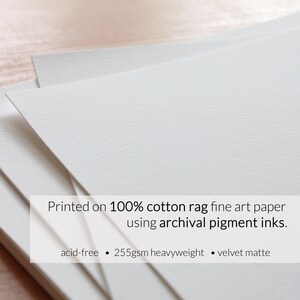 May include: Close-up of a stack of white, textured, fine art paper. The paper is 100% cotton rag, acid-free, 255gsm heavyweight, and has a velvet matte finish. The text "Printed on 100% cotton rag fine art paper using archival pigment inks." is printed on the paper.
