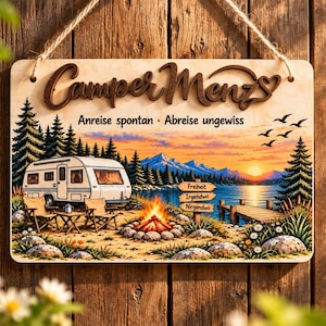 Könnte beinhalten: Ein rechteckiges Holzschild zum Aufhängen mit dem Text CamperMenzs und Anreise spontan - Abreise ungewiss. Die Illustration zeigt einen weißen Wohnwagen, zwei Stühle, ein Lagerfeuer, einen See, Berge und ein Schild mit Freiheit, Irgendwo, Nirgendwo.