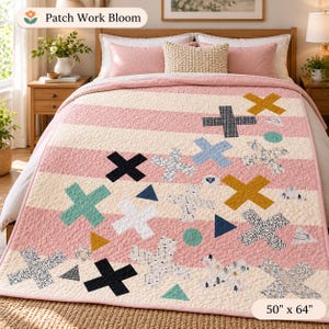 May include: A quilt featuring horizontal pink and cream stripes decorated with various patterned and solid-coloured X shapes, triangles, and circles. The quilt measures 127 cm by 163 cm and includes the text Patch Work Bloom.