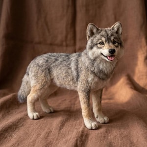 May include: A needle-felted wolf figurine featuring a realistic coat of grey, brown, and white fur. The wolf is depicted in a standing position with its mouth slightly open, revealing a pink tongue, and its ears are pointed upward.