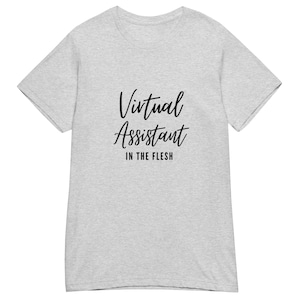 Könnte beinhalten: Ein hellgrau meliertes Kurzarm-T-Shirt mit dem schwarzen Schriftzug Virtual Assistant in einer kursiven Schreibschrift, wobei die Worte IN THE FLESH in einer fetten, serifenlosen Großbuchstabenschrift direkt darunter gedruckt sind.