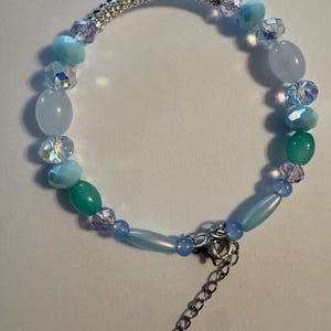 May include: A beaded bracelet featuring a variety of light blue, turquoise, and clear faceted crystal beads, interspersed with smooth oval beads and a textured silver-toned metal segment, finished with a silver-toned lobster clasp and chain.