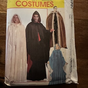 May include: A sewing pattern for three different costumes: a white hooded cloak, a black hooded cloak with red trim, and a blue hooded cloak with white trim. The pattern is titled "McCall's Costumes" and has the number "M5957" printed on it.